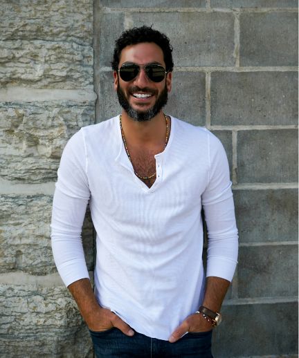 Keith Mercurio in sunglasses and a white long-sleeved shirt standing in front of a stone building and smiling at camera