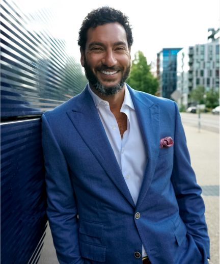 Keith Mercurio in blue suit leaning against a building and smiling at camera